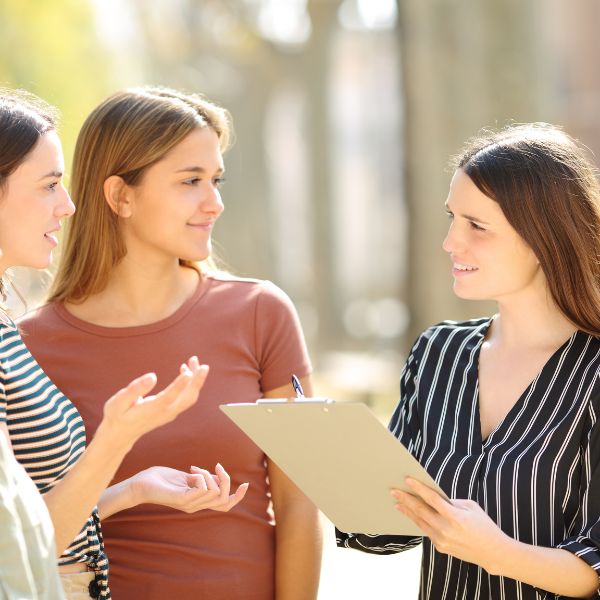 Image shows three women with two women providing opinion and the woman on the right holding a notepad and taking notes