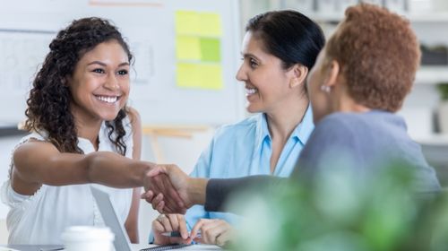 Woman with a big smile shaking hands with another person on getting a job offer